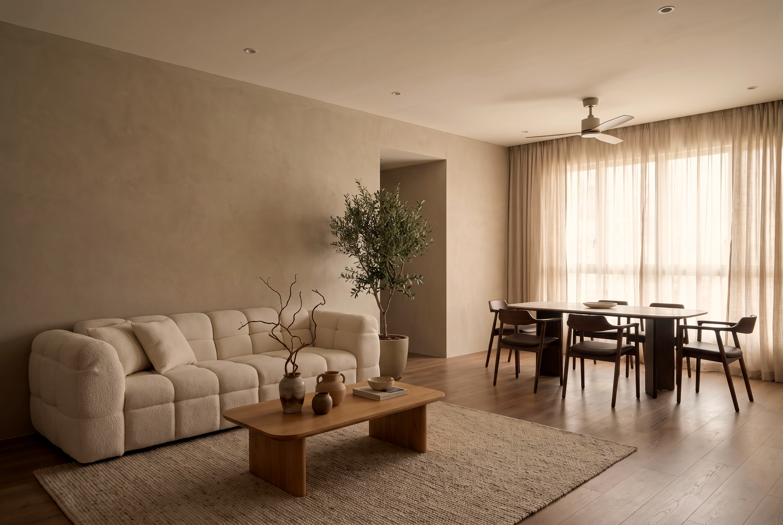 An open-plan living and dining room: a cream boucl&eacute; Son&Bear sofa and wood coffee table on a jute rug, an olive tree, and a wood dining set by sheer-curtained windows.
